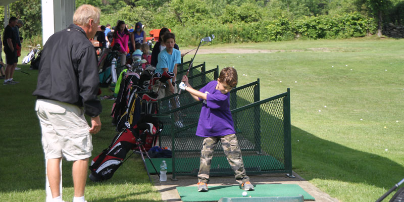 Photo of John Lawton giving golf lessons on the range at Junior Golf Camp.
